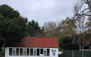 Screenshot the old crumbling bowling club building pavillion in white with a red roof